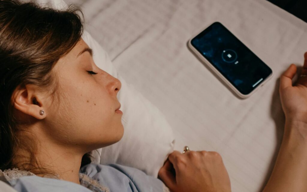 Mobilni telefon na krevetu pored žene koja spava
